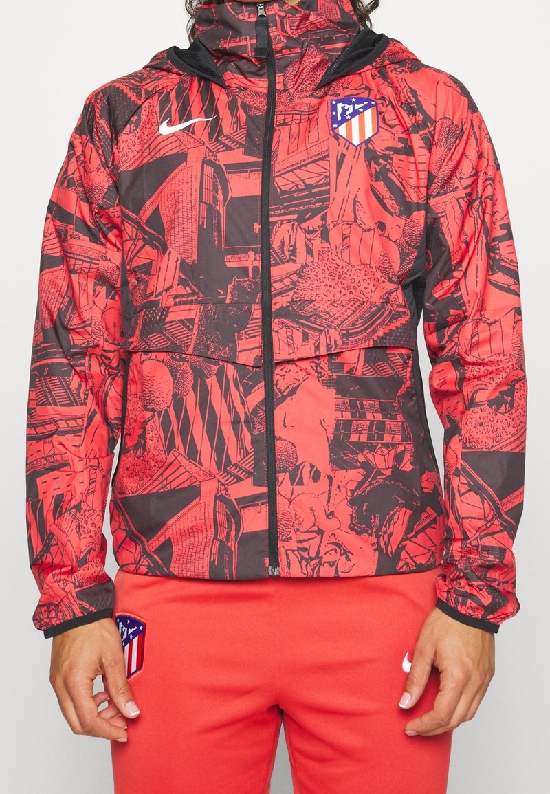 Veste zippée à motif rouge et noir avec le logo de l'Atlético Madrid sur la poitrine et pantalon rouge assorti avec les logos de l'Atlético Madrid et de Nike.