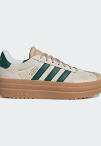 Sneaker Adidas in suede beige con strisce in pelle verde, suola marrone chiaro e lacci di colore chiaro. Presenta superfici testurizzate e dettagli del logo.