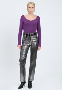 Lila Langarmshirt, metallic-silberne hochtaillierte Hose mit einem schwarzen Gürtel mit Metalldurchzügen und schwarzen Absatzstiefeln bis zum Knöchel.