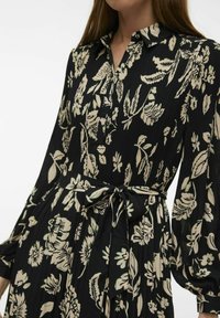 Robe noire à motifs floraux avec un col, des manches bouffantes longues et une ceinture à nouer. Le tissu présente une texture côtelée agrémentée d'imprimés floraux crème.