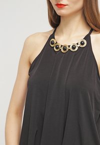 Top halter nero con un design fluido, caratterizzato da una collana in tono oro con sei pietre nere rotonde come accento principale.
