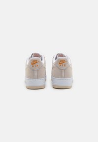 Sneakers Nike Air beige con suola bianca, texture in suede e dettagli arancioni sul tallone. Design minimalista (vista posteriore).