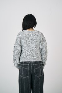 Világosszürke, textúrált kötött pulóver, laza szabással és bordázott aljúval, fekete, bő szárú farmernadrággal, amely két hátsó zsebbel rendelkezik.