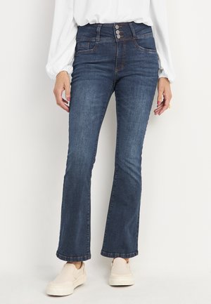 Donkerblauwe flared jeans met een hoge taille, voorzien van drie voorknopen, twee zijzakken en een gladde denimtextuur. G gedragen met beige instapschoenen.
