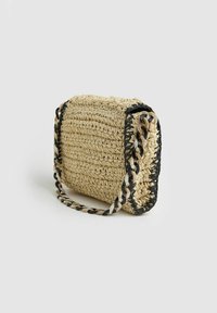 Piccola borsa rettangolare beige intrecciata con rifiniture nere e una catena spessa beige, nera e bianca su uno sfondo bianco.
