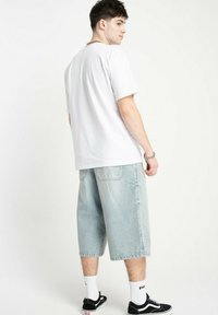 Biała bawełniana koszulka w połączeniu z jasnoniebieskimi dżinsowymi szortami, charakteryzującymi się luźnym krojem i długością do kolan. Czarne trampki z białymi akcentami.