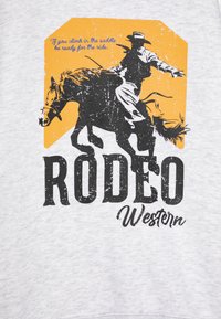 Camicia grigia con una grafica in stile vintage di un cowboy a cavallo su uno sfondo giallo. Il testo dice "RODEO" e "Western."