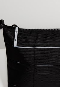 Borsa in tessuto nero intrecciato con chiusura a zip, caratterizzata da righe orizzontali e una striscia lucida. Materiale resistente e forma strutturata.