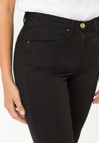 Jeans in denim nero con un design a vita alta e una vestibilità slim, dotati di cinque tasche e dettagli in metallo dorato. Tessuto liscio con dettagli cuciti.