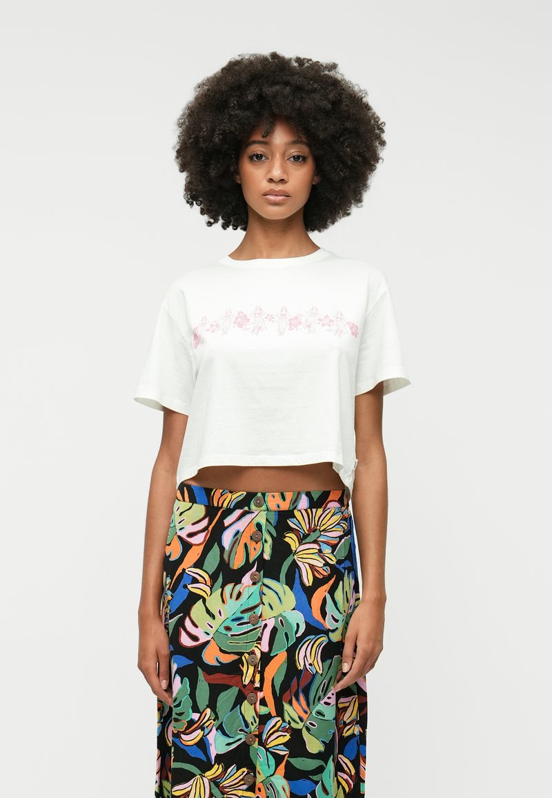 White cropped T-shirt with pink floral print, paired with a long black skirt featuring colorful leaf patterns and button details.