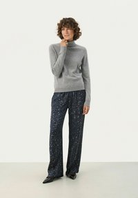 Helles graues, langärmliges Rollkragensweatshirt kombiniert mit dunkelblauen, gemusterten weit geschnittenen Hosen mit einem dezenten Tierdruck. Schwarze Schuhe.