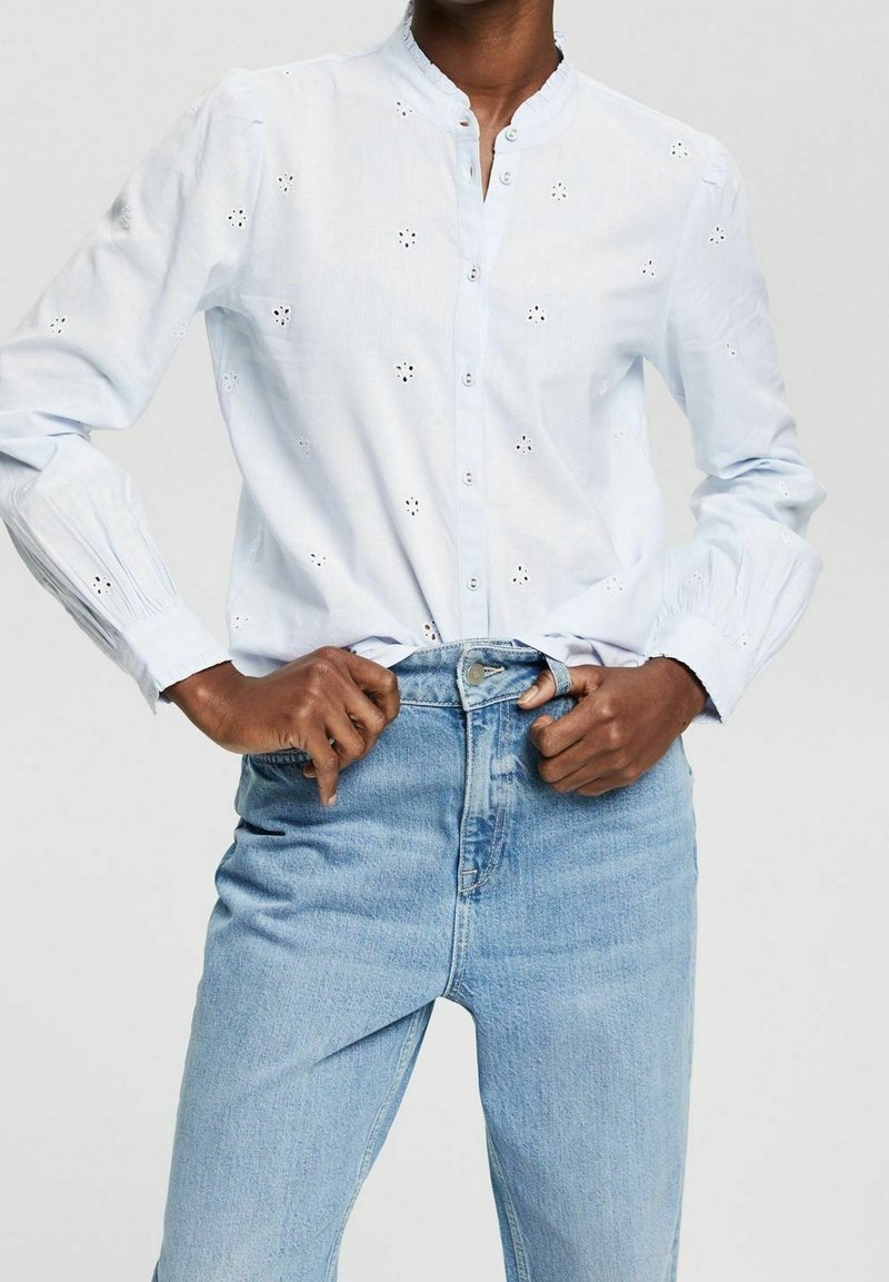 Camicia azzurra chiaro con colletto alla mandarino, caratterizzata da dettagli floreali ricamati e maniche lunghe, abbinata a jeans in denim a vita alta.