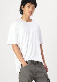 Λευκό βαμβακερό T-shirt με κοντά μανίκια, στρογγυλή λαιμόκοψη και χαλαρή εφαρμογή, συνδυασμένο με γκρι cargo παντελόνι που διαθέτει τσέπες και λεπτομέρεια με φερμουάρ.