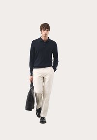 Marineblaues Langarm-Polohemd, cremefarbene Hose, schwarze Schuhe und eine schwarze Tragetasche. Schlichtes Design, glatte Textur, minimale Akzente.