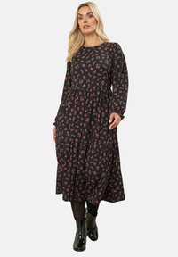 Svart blommig klänning med långa ärmar, med ett åtsittande liv och flarnad kjol, dekorerad med små röda och rosa blommor.