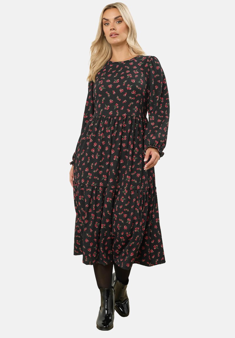 Svart blommig klänning med långa ärmar, med ett åtsittande liv och flarnad kjol, dekorerad med små röda och rosa blommor.