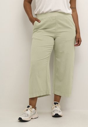 Pantaloni larghi verde chiaro con vita elastica, tessuto texturizzato e tasche laterali, abbinati a sneakers bianche e grigie.
