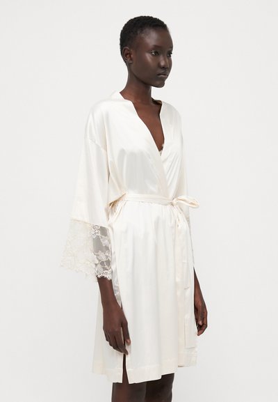 Robe di seta avorio con maniche bordate in pizzo, design avvolgente e chiusura con cravatta. Presenta spacchi laterali per un maggiore fluire ed eleganza.