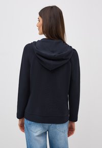 Sweat-shirt à capuche bleu marine en tissu texturé, présentant une coupe ample, des manches longues et une doublure douce. Associé à un jean bleu clair.