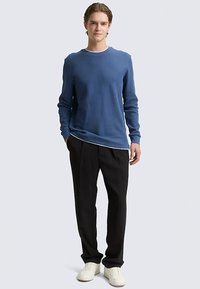 Blaues, geripptes Langarmshirt mit rundem Ausschnitt, kombiniert mit schwarzen Hosen und weißen Sneakers. Schlichtes, figurbetontes Design.