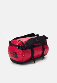Red duffel bag made of durable fabric with black accents. Features adjustable straps, a large compartment, and black logo print.