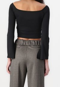 Schwarzes Langarmshirt mit schulterfreiem Ausschnitt, kombiniert mit karierten, hochgeschnittenen Hosen mit elastischem Bund.