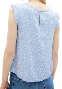 Jasnoniebieska bluzka z białym kwiatowym wzorem, krótkimi rękawami, zaokrąglonym dołem i zapięciem na guziki z tyłu. Teksturowana, miękka tkanina.