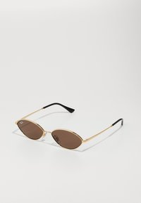 Ochelari de soare cu ramă din metal auriu, cu lentile ovale de culoare brună, având brațe subțiri și vârfuri negre. Include detaliu cu logo pe lentilă.