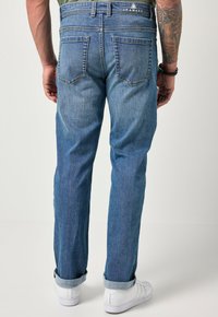 Jeans de mezclilla azul claro con corte recto, dos bolsillos traseros y puños remangados; textura lisa con un desvanecimiento mínimo.