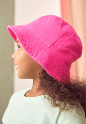 Růžový bavlněný klobouk s širokou krempou, texturovanou tkaninou a prošívanými detaily, nošený dítětem s kudrnatými vlasy, pohled ze strany.