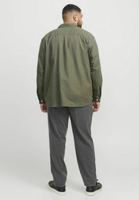 Cămașă butonată de culoare verde măslinie, cu o suprafață ușor texturată, hem rotunjit și mâneci lungi, asortată cu pantaloni gri cu dungi și adidași negri.