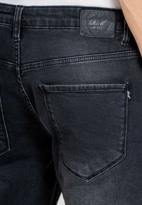Jeans de mezclilla negra con un corte ajustado, diseño de cinco bolsillos y un parche de cuero texturizado en la cinturilla con el nombre de la marca.