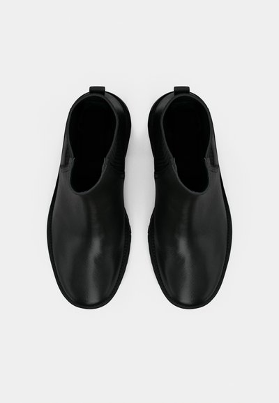 Bottes basses en cuir noir avec une texture lisse, un bout arrondi, des panneaux latéraux élastiques et des onglets pour faciliter l'enfilage.