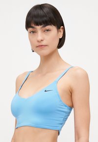 Šviesiai mėlynas sportinis liemenukas su V formos iškirpte, reguliuojamomis petnešėlėmis ir juodu Nike logo kairėje pusėje. Lygi, elastinga medžiaga.