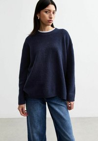 Pull en maille bleu marine avec un col rond, des épaules tombantes et une coupe décontractée. Associé à un jean en denim bleu clair.