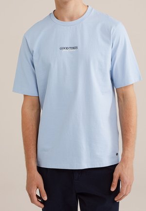 Homme portant un t-shirt bleu clair à manches courtes avec le texte "GOOD TIMES" imprimé en noir sur la poitrine.