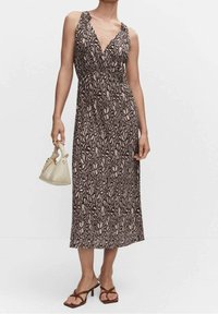Robe maxi marron foncé avec un motif floral, dotée d'un décolleté en V, de bretelles spaghetti et d'une silhouette fluide. Portée avec des sandales plates.