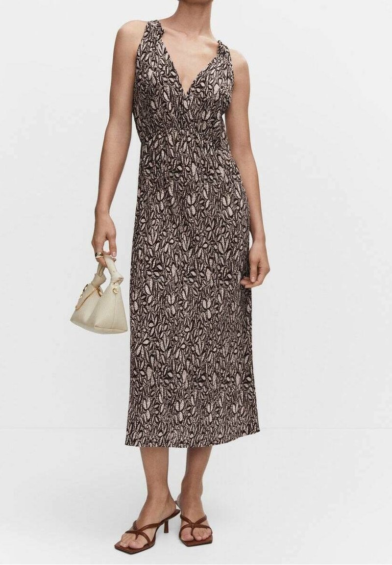 Robe maxi marron foncé avec un motif floral, dotée d'un décolleté en V, de bretelles spaghetti et d'une silhouette fluide. Portée avec des sandales plates.