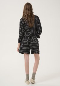 Černý vzorovaný outfit s dlouhými rukávy a šortkami, který má abstraktní bílé linie a spirály. Měkká tkanina, uvolněný střih, neformální design.