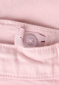 Lys rosa stoff med jevn tekstur som har en rund plastknapp og en stoffløkke for å feste. Synlige sømdetaljer.