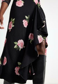 Abito nero floreale con rose rosa, tessuto testurizzato, orlo arricciato e uno spacco alto, abbinato a stivali neri lucidi fino al ginocchio.