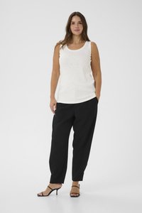 Weißes ärmelloses Oberteil mit glitzernden Akzenten, kombiniert mit lockeren schwarzen Hosen. Das Model trägt schwarze Riemchensandalen. Schlichtes, modernes Design.