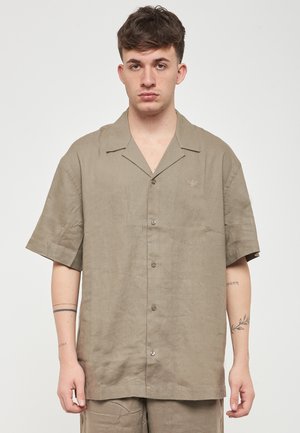 Camicia a maniche corte con colletto realizzata in leggero tessuto beige testurizzato con una sottile lucentezza, con chiusura a bottoni e piccolo logo decorativo.