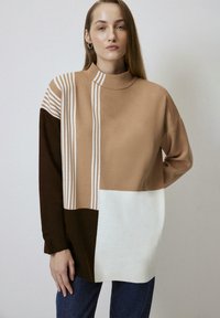 Crème, bruin en camel kleurgeblokte trui met verticale witte strepen; hoge hals, lange mouwen, zachte textuur en een losse pasvorm.