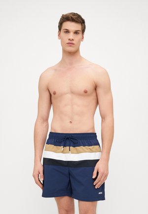 Marineblaue Schwimmshorts mit einem Kordelzugbund zeigen horizontale Streifen in Beige, Weiß und Schwarz. Der Stoff wirkt leicht und glatt.