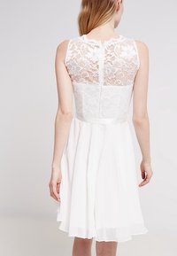 Vit klänning med spetsbak och en mjuk, flödande kjol. Designen har en figursydd bodice och en subtil midjebanddetalj.