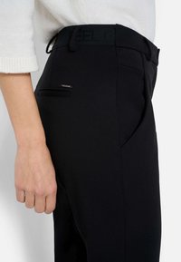 Czarne dopasowane spodnie o gładkiej fakturze, z szlufkami na pasek i dyskretną tylną kieszenią z metalowym dodatkiem.
