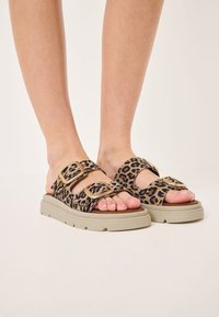 Leopard print slide sandals with double buckle straps, beige platform sole, and textured material. Open-toe design for breathability.