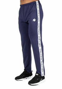 Marineblauwe sportbroek met witte zijstrepen met de tekst "GORILLA WEAR." Elastische tailleband en ritszakken. Gekocht met zwarte sportschoenen.