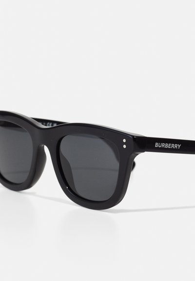 Černé sluneční brýle s masivním plastovým rámem, tmavými skly, dvěma malými stříbrnými tečkami poblíž pantů a logem "BURBERRY" na rameni.